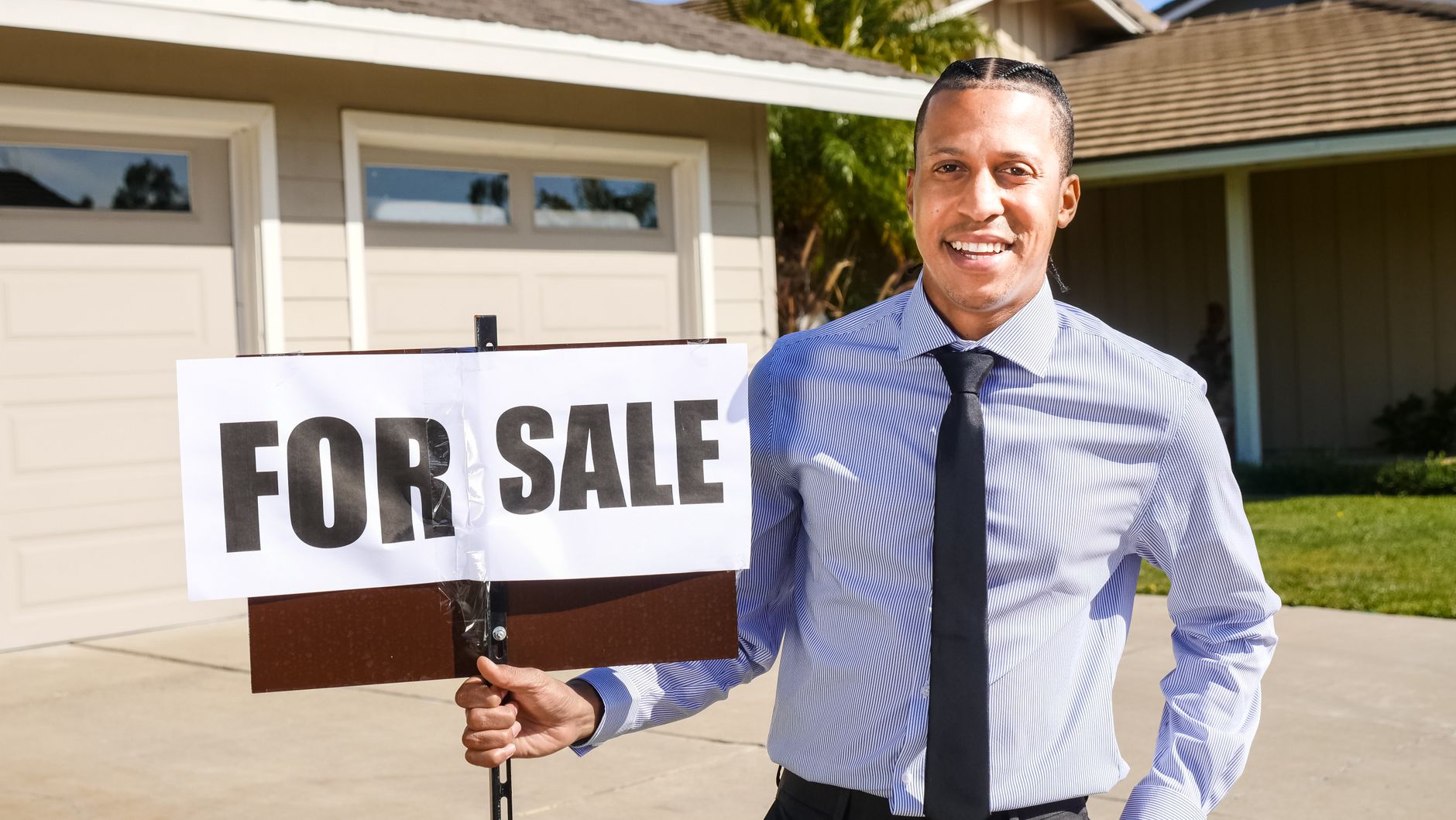 Real estate agent holding a For Sale sign in front of a listed home